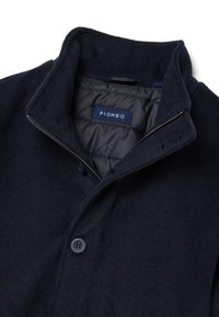 Marineblauer Mantel aus Wollmischung mit hohem Kragen, Reißverschluss vorne und Details mit zwei Knöpfen. Das Innere ist mit gestepptem Futter versehen. Das Markenetikett ist sichtbar.