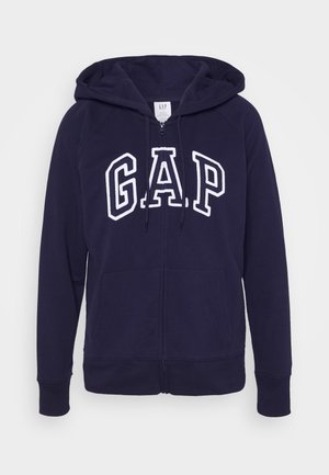 Granatowa bluza rozpinana na zamek z przednimi kieszeniami, kapturem ze sznurkiem oraz białym logo "GAP" na wysokości klatki piersiowej.