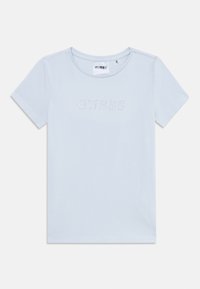 T-shirt bleu clair à manches courtes en coton doux. Il possède un col arrondi et le mot "GUESS" en ornementations en cristaux sur le devant.