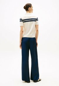 Beige polo skjorte med marineblå striber, parret med løstsiddende marineblå bukser. Glat tekstur; afslappet pasform; sandaler med et enkelt design.
