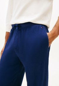 I pantaloni texturizzati blu navy presentano un elastico in vita con cordoncino e tasche, con un piccolo logo sul lato. Il tessuto ha una finitura a coste.