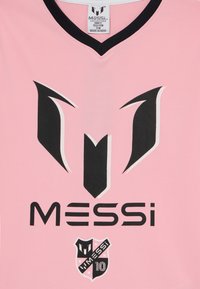Camiseta deportiva rosa con un cuello en V negro. Presenta un logotipo negro prominente y el nombre "MESSI" en letras negritas, junto con un emblema de escudo.