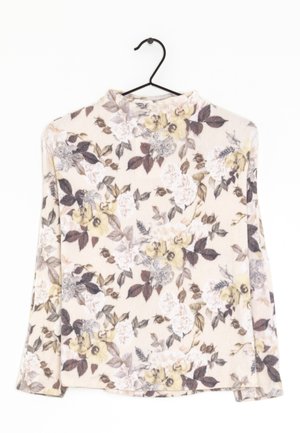 Maglietta beige a maniche lunghe con motivi floreali gialli e marroni appesa a una gruccia nera su sfondo bianco.