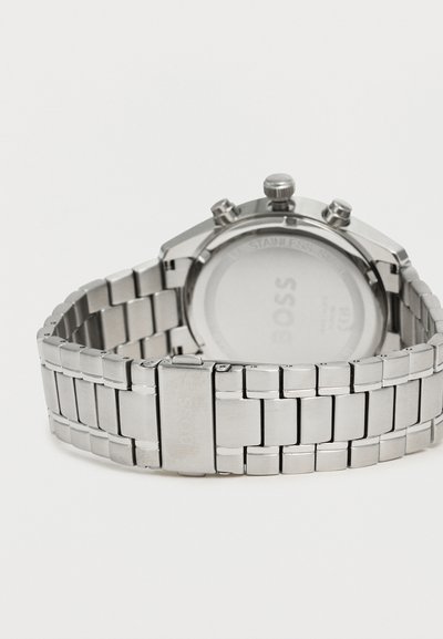Bracelet de montre à maillons en métal argenté avec une boucle, attaché à l'arrière d'un boîtier de montre chronographe rond en acier inoxydable.