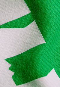 Textil que presenta un diseño abstracto verde y dentado sobre un fondo blanco, con una textura tejida y colores contrastantes claros.