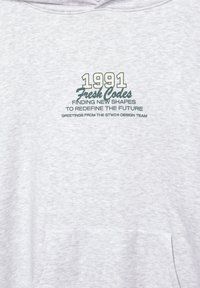 Felpa grigia realizzata in tessuto morbido con una stampa che presenta il testo verde "1991 Fresh Codes" e del testo aggiuntivo sottostante.