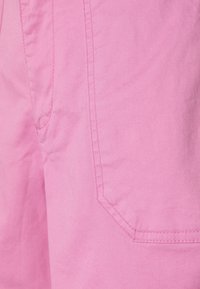 Shorts en tissu rose à texture lisse, avec une poche latérale et des coutures contrastées. Le matériau semble léger et respirant.