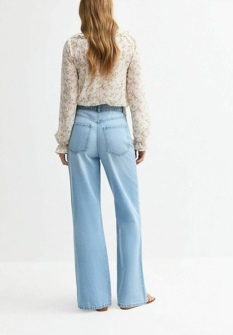 Vaqueros de pierna ancha azul claro, confeccionados en denim con una cintura alta, que presentan dos bolsillos traseros y un acabado suave y texturizado. Combinados con una blusa floral.