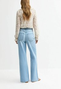 Jasnoniebieskie dżinsy o szerokich nogawkach, wykonane z denimu, z wysokim stanem, czterema kieszeniami i delikatną teksturą. Noszone z bluzką w kwiatowy wzór.