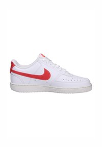 Baskets blanches en matériau lisse, avec un swoosh rouge et un capuchon de talon. Elles possèdent une semelle blanche texturée avec des trous de ventilation sur la boîte à orteils.