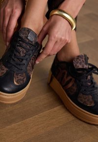 Schwarze und braune Leopardenmuster-Plateausneaker aus strukturiertem Leder mit kontrastierenden Gummisohlen, ausgestattet mit schwarzen Schnürsenkeln und Logo-Akzenten.