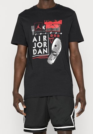 Black Air Jordan t-shirt with red and white graphic including sneaker sole, Jumpman logo, and text "Air Jordan 23" worn with black shorts.