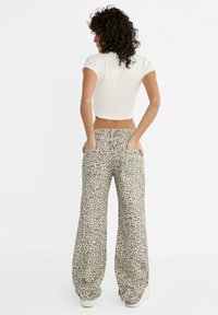 Pantalones de pierna ancha con estampado de leopardo en beige claro y marrón, con dos bolsillos traseros y cintura de talle medio. Tela elástica y suave con un ajuste relajado.