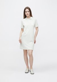 Polojurk van lichtbeige katoen, tot op de knie, met korte mouwen, voorzien van een klassieke kraag en een recht model, gecombineerd met grijze instappers.