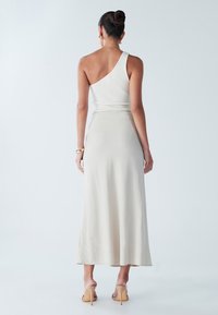 Haut blanc côtelé à une épaule assorti à une jupe midi fluide crème, caractérisée par une texture douce et une fente arrière, porté avec des sandales à talons nude.