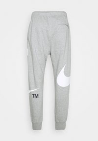 Šedé tepláky z měkkého materiálu s velkým bílým logem Nike a menším černým textem, s elastickým pasem a lemy.