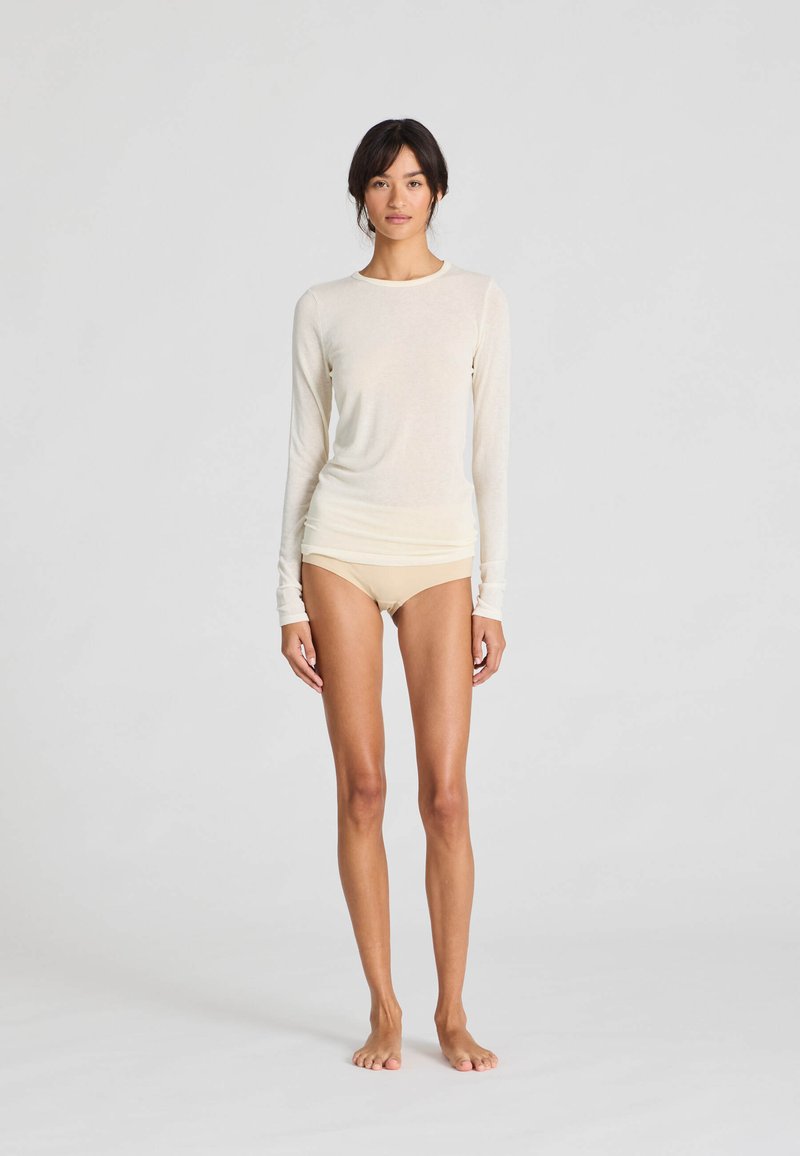 Långärmad krämfärgad topp i mjukt tyg, kombinerad med ljusbeige boyshorts med en åtsittande design och minimala sömmar.