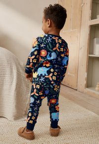 Kleurrijk pyjama set met lange mouwen, voorzien van bloem- en dierenpatronen op een marineblauwe achtergrond. Zachte stof met geribbelde manchetten en aansluitende pijpen.