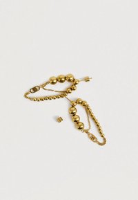 Náušnice zlatého řetízku s korálky různých velikostí a malým odnímatelným uzávěrem na světlém jednobarevném pozadí.