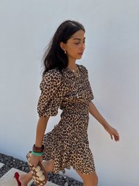 Leopardprint jurk met korte pofmouwen en een gerimpelde zoom. Accessoires zijn onder andere een geweven clutch met ronde accenten en meerkleurige armbanden.