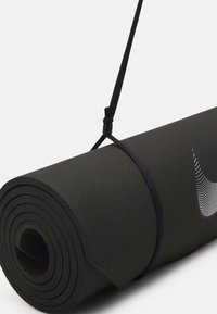 Esterilla de yoga negra enrollada de forma ajustada con una superficie texturizada, asegurada por una correa negra. Presenta un logo blanco de Nike en el lateral.