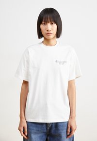 Hvid bomulds t-shirt med rund hals og korte ærmer. Har et lille, broderet logo på venstre bryst og en afslappet pasform.