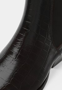 Bota de couro castanho com uma textura brilhante e padrão de crocodilo. Painéis laterais elásticos e um salto afunilado realçam o design elegante.