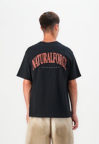 Sort bomulds t-shirt med et stort rødt vintage-agtigt graphic "NATURALFORCE" på ryggen. Korte ærmer og en afslappet pasform.