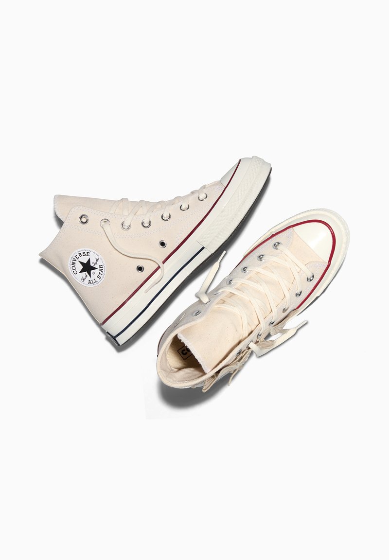 Paar off-white Converse All Star High-Top-Sneaker mit roten und schwarzen Streifen auf der Gummisohle, auf weißem Hintergrund platziert.