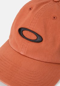 Cappellino da baseball in cotone arancione con visiera curva e logo nero ricamato sulla parte anteriore. Tessuto testurizzato con dettagli di cucitura ben visibili.