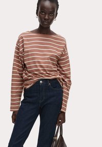 Bruin en wit gestreepte lange mouwen shirt gecombineerd met donkerblauwe jeans. Model met een donkere handtas die casual kleding toont.