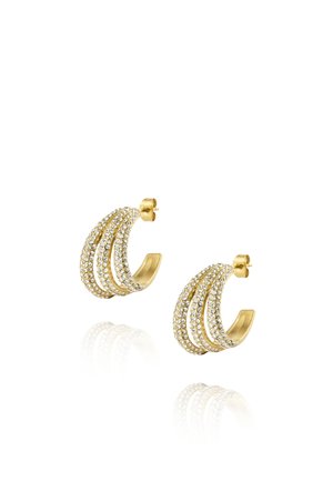 Boucles d'oreilles créoles dorées avec trois rangées de petits cristaux clairs, reflétant sur une surface blanche.