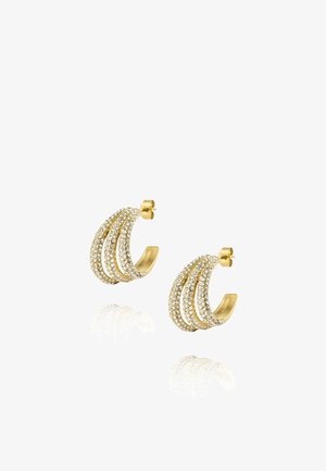 Boucles d'oreilles créoles dorées avec trois rangées de petits cristaux clairs, reflétant sur une surface blanche.