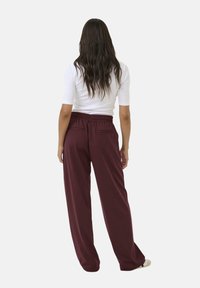 Bordeauxfarbene Sweatpants mit entspannter Passform, elastischem Bund und zwei Gesäßtaschen, kombiniert mit einem enganliegenden weißen Oberteil. Glatte Textur.