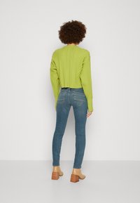 Suéter corto de punto trenzado en verde claro con mangas largas, combinado con jeans ajustados de color azul y botas de tobillo de tacón cuadrado en color beige.
