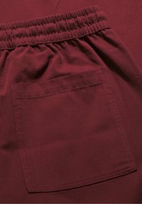 Zbliżenie na bordową elastyczną talię i kwadratową tylną kieszeń na tkaninie, podkreślające szycie i teksturę.