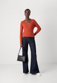 Red cable-knit sweater with V-neck, paired with dark flared jeans and white sneakers. Black handbag with short handle. Smooth texture.