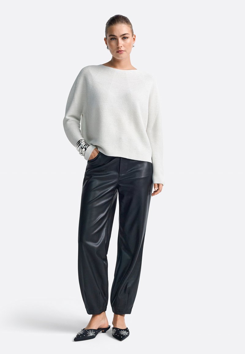 White textured knit sweater with a wide neckline, paired with black faux leather trousers featuring a loose fit and cuffed ankles. Black embellished mules.