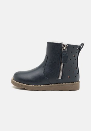 Botas de tornozelo azul-marinho com acabamento em imitação de couro texturizado, fecho lateral, e recortes em forma de estrela no calcanhar exterior, apresentando uma sola de borracha bege.
