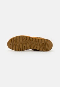 Brown rubber outsole with a textured tread pattern, featuring deep grooves and various traction lugs, indicating durable outdoor use.