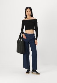 Černý crop top s odhalenými rameny, džíny s vysokým pasem a černé tenisky s bílými pruhy. Nese černou látkovou tašku.