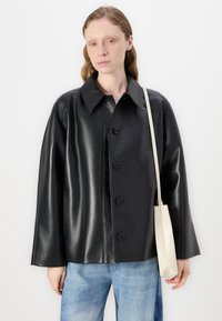 Chaqueta de piel sintética negra con un collar en punta, cierre de botones y bolsillos laterales, llevada sobre unos pantalones de mezclilla azul claro.