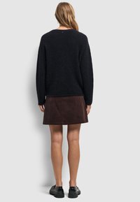 Zwarte trui gemaakt van zacht materiaal, gecombineerd met een bruine corduroy rok. De outfit bevat zwarte chunky schoenen, met een ontspannen pasvorm en een achteraanzicht.