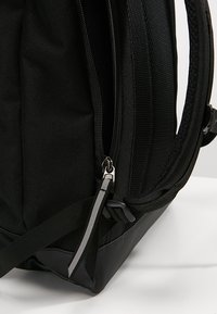 Mochila negra con un acabado de tela texturizada, que cuenta con un compartimento con cremallera, correas de hombro acolchadas y un material base duradero.