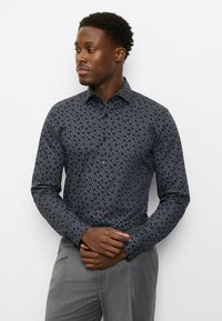 Dunkel gemustertes Hemd mit floralem Design in Marineblau und Grau, mit Button-Down-Kragen und langen Ärmeln. Graue Hose.