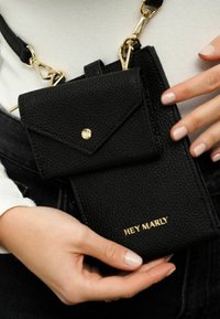 Schwarze strukturierte Leder-Crossbody-Tasche mit einem abnehmbaren kleineren Beutel, goldenen Beschlägen und dem eingeprägten Markenlogo auf der Vorderseite.