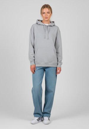 Lichtgrijze hoodie met een trekkoordkap, een kangoeroezak en ribgebreide manchet, gecombineerd met blauwe wijde jeans en witte sneakers.