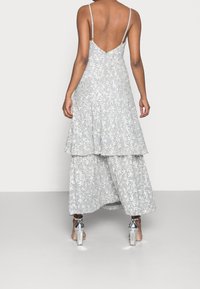 Jasnoszara sukienka maxi z warstwowym wzorem, skomplikowanym haftem kwiatowym, regulowanymi cienkimi ramiączkami i niskim tyłem. Połączona z srebrnymi szpilkami.