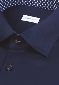 Marineblauw overhemd met knopen en een gestructureerde kraag, voorzien van een wit label en een gewatteerde binnenzijde met lichtblauwe stippen.