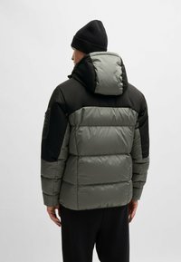 Puffer jacket with a hood in dark green and black. Padded design, smooth texture, adjustable features, and a zippered pocket on the sleeve.
